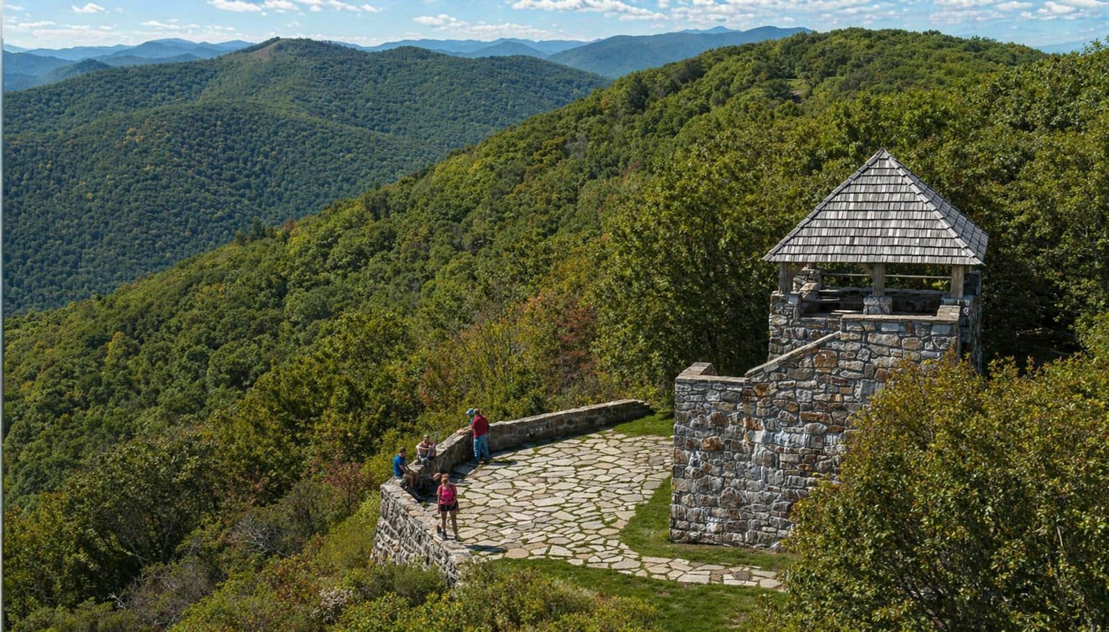 Scenic mountain landscape in Franklin, NC with a stone lookout tower and hikers enjoying the view.