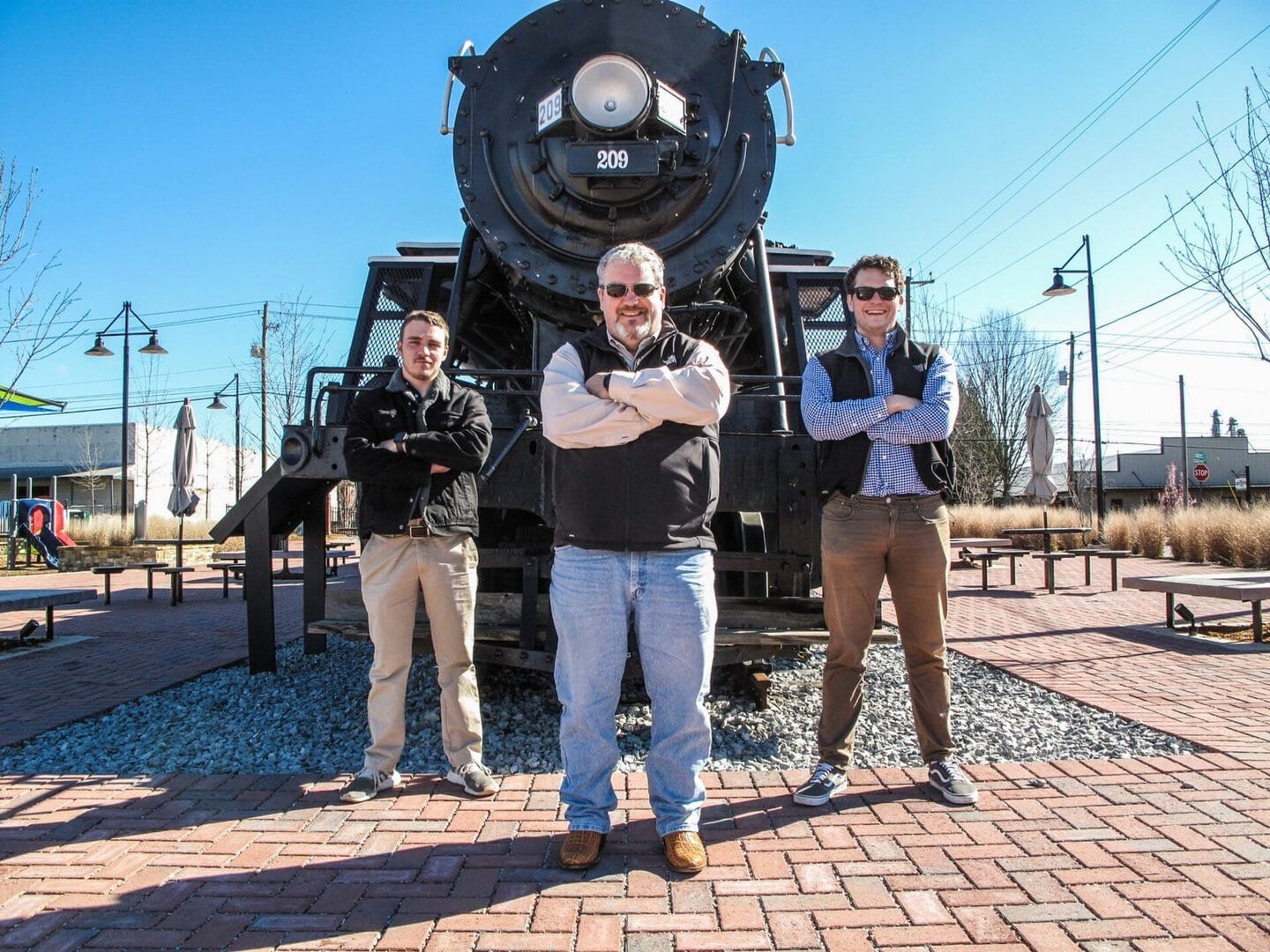 Team of three professionals posing confidently in front of a historic locomotive.