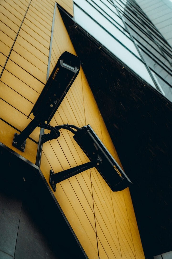 Security cameras mounted on a yellow building exterior for surveillance.